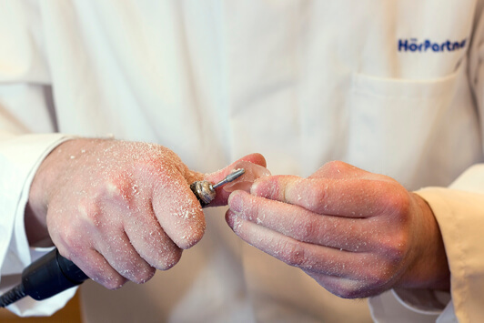 Ein Hörakustiker schleift ein Ohrpassstück mit Präzisionswerkzeug in der Werkstatt.